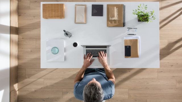 Top view, a man sitting at tidy desk and working on his laptop