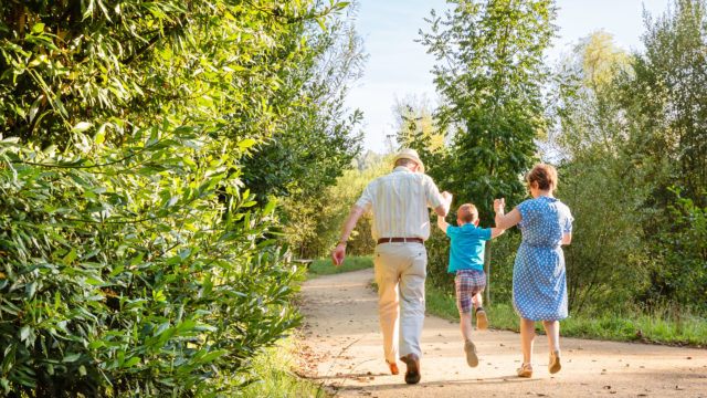 Back view of grandparents and grandchild jumping on a nature path