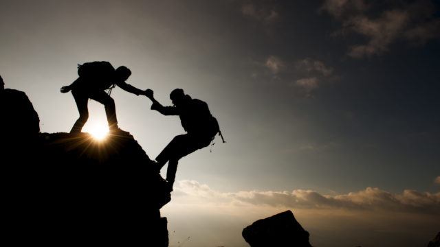 One man helps another climb a mountain