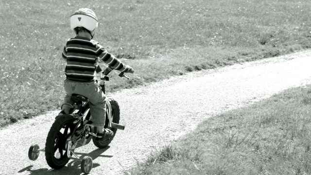 Small boy is prepared to ride his bike as he sets out on a path that leads out of the picture
