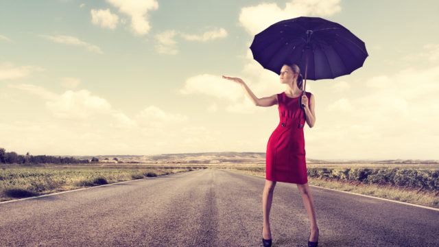 Stylish female with umbrella standing on highway at sunny day