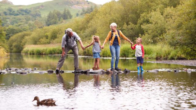 grandparents and grandchildren crossing the river while hiking