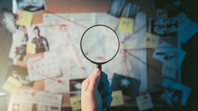 hand holding magnifying glass over documents