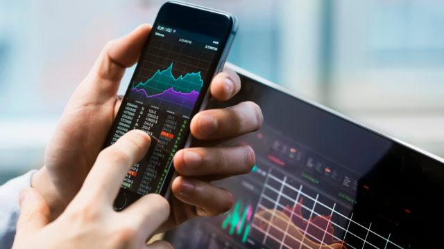 man holding phone with stocks app open