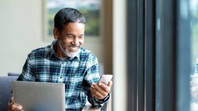 man happily looking at phone and laptop