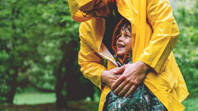 man wrapping a raincoat around his child