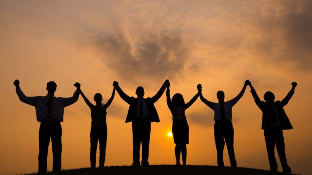 team raising hands with sunset background