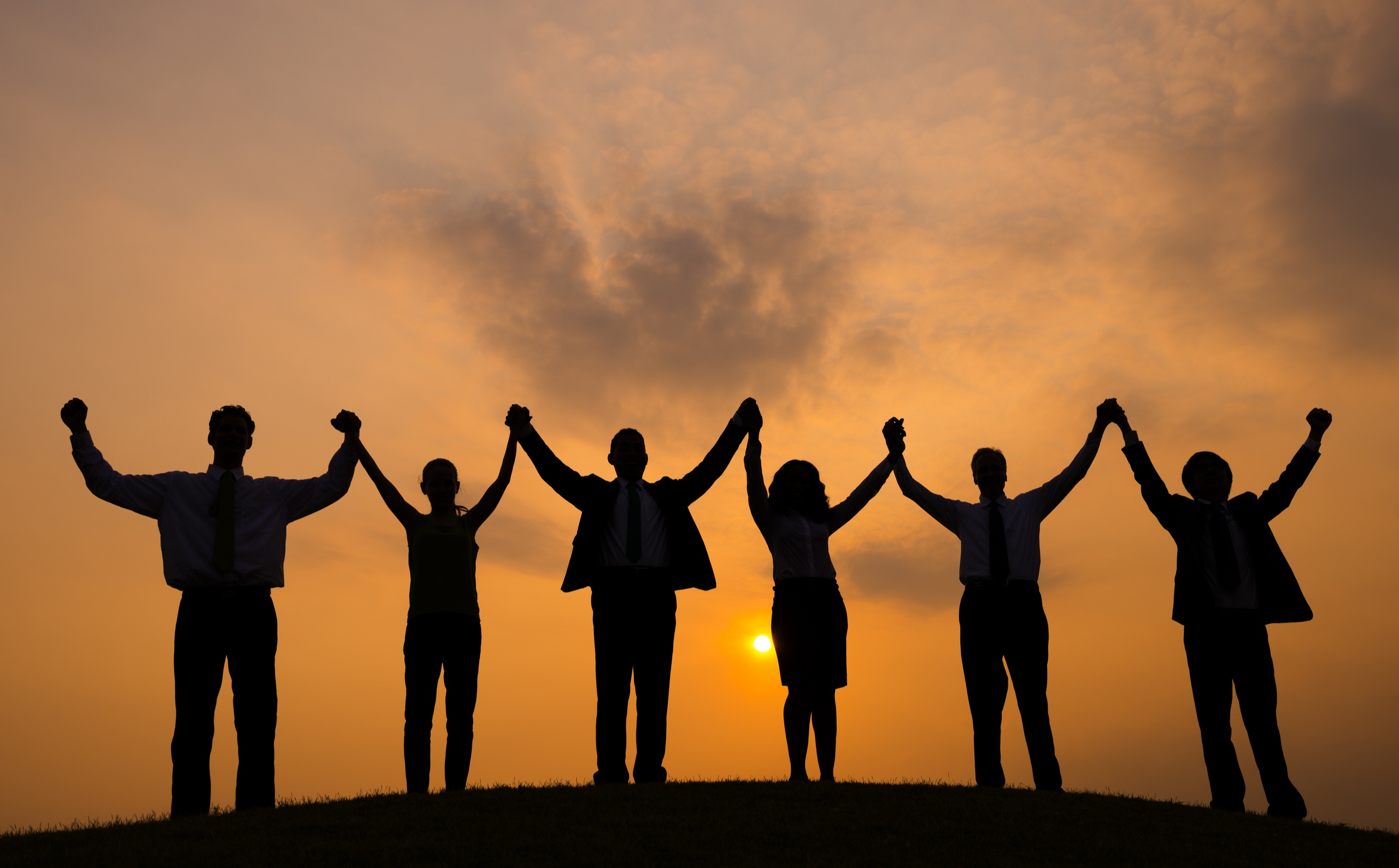 team raising hands with sunset background