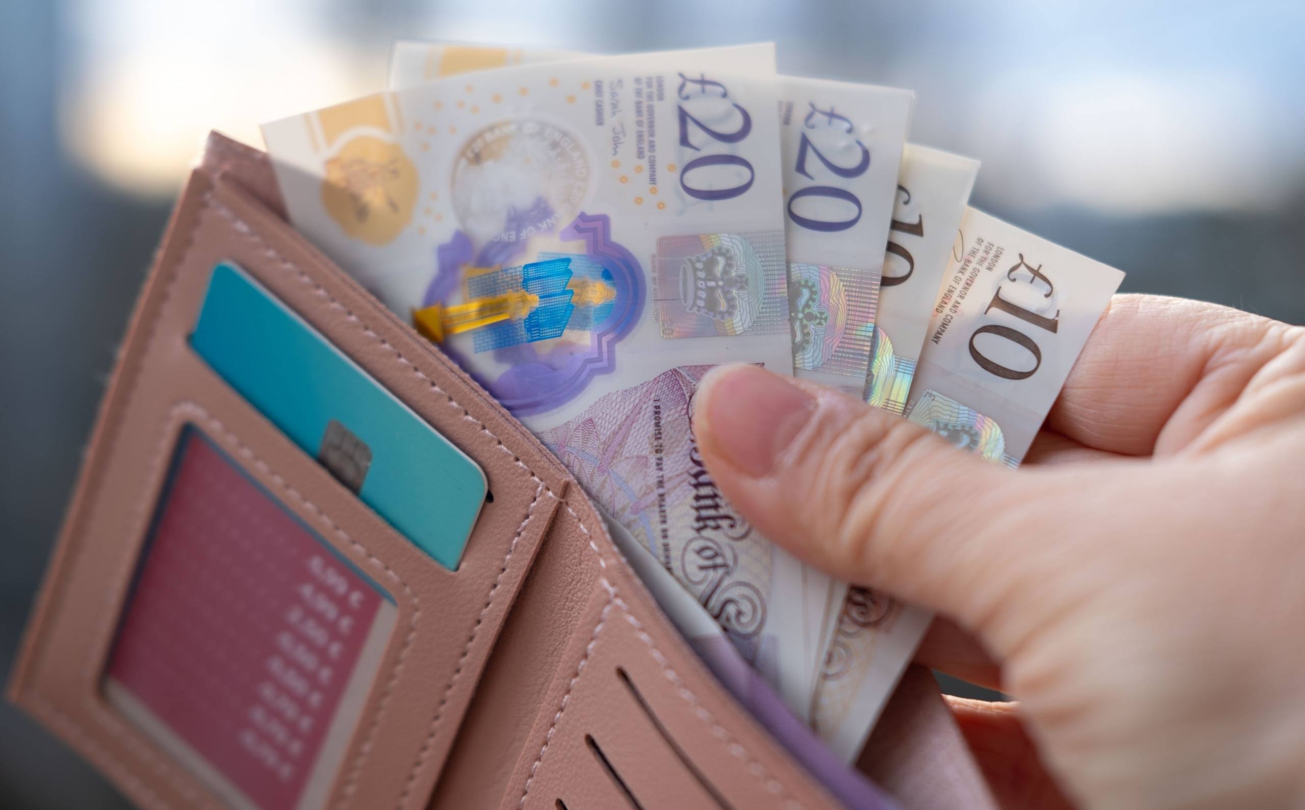 person holding wallet full of £20 and £10 notes