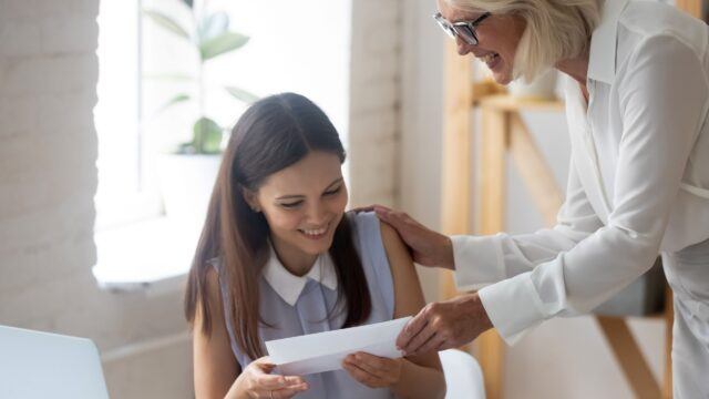An older woman handing a young woman an envelope