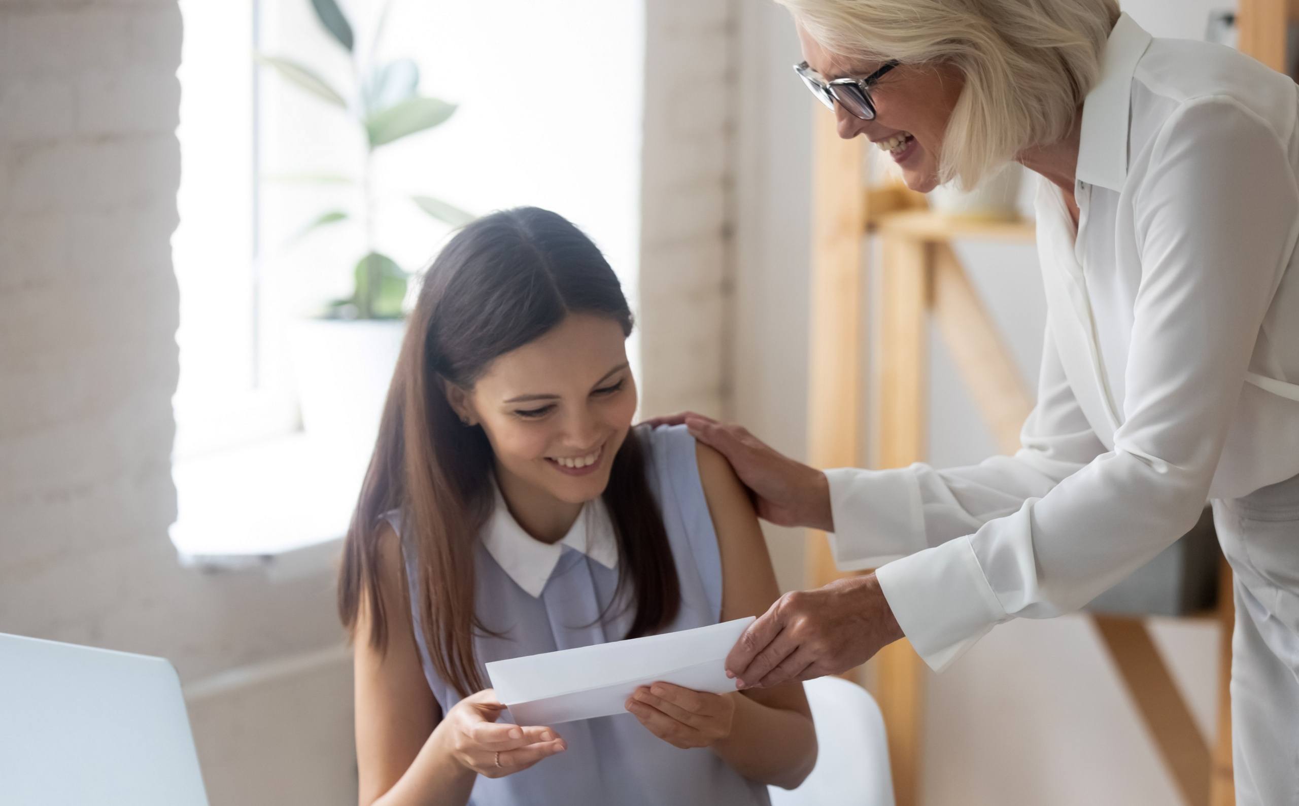 An older woman handing a young woman an envelope