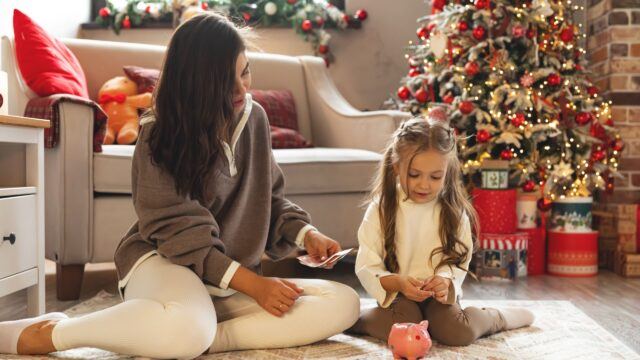 2 fantastic ways to invest for children and help set them up for life Happy mother giving money to her daughter for piggy bank.